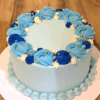 Blue Bliss Birthday Cake with royal blue and sky-blue cream swirls topped with golden pearls on a wooden background.