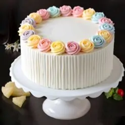 Pastel rose vanilla cake with colorful floral icing decorations, available for birthday and anniversary delivery in Guwahati.